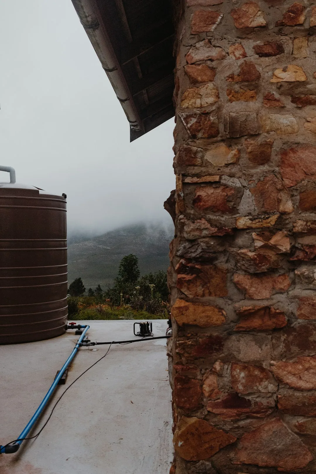 A slim grey rainwater tank beside a house wall with a downpipe filter feeding into it