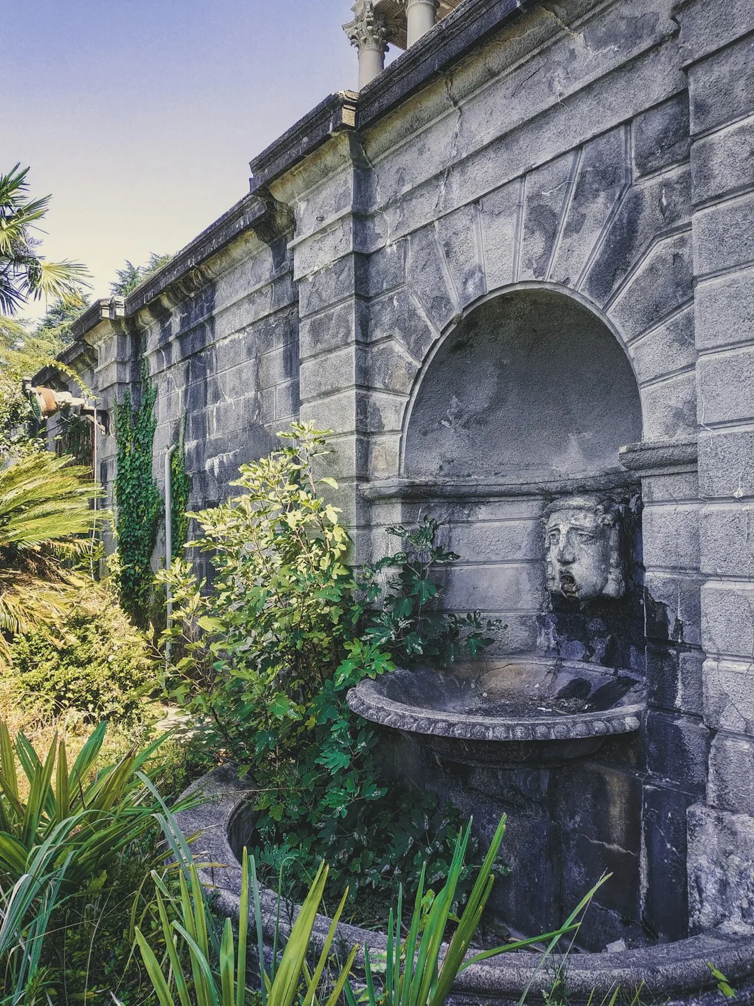 A compact rainwater tank tucked into the corner of a paved city garden beside potted shrubs